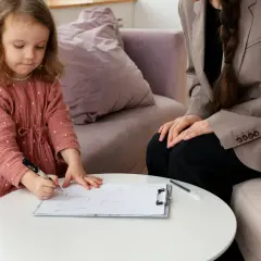 Mała dziewczynka rysuje na kartce, podczas gdy dorosła kobieta obserwuje. Sesja terapeutyczna ados 2.