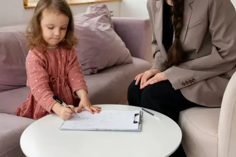 Mała dziewczynka rysuje na kartce, podczas gdy dorosła kobieta obserwuje. Sesja terapeutyczna ados 2.